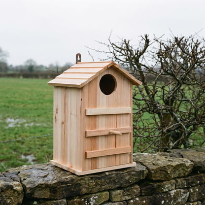 The owl box standing on a dry-stone wall with a hedgerow behind